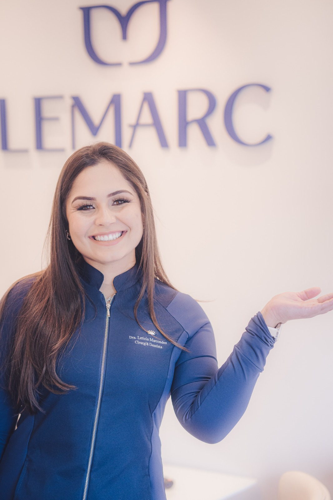 Dra. Letícia Marcondes na recepção da Lemarc Odontologia, diante da marca da clínica